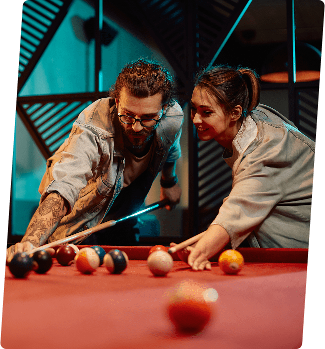 A man and woman play pool on a red table, focusing on their shots.